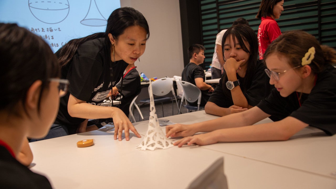 Girls and a lady gathering around a table looking at a tall white object