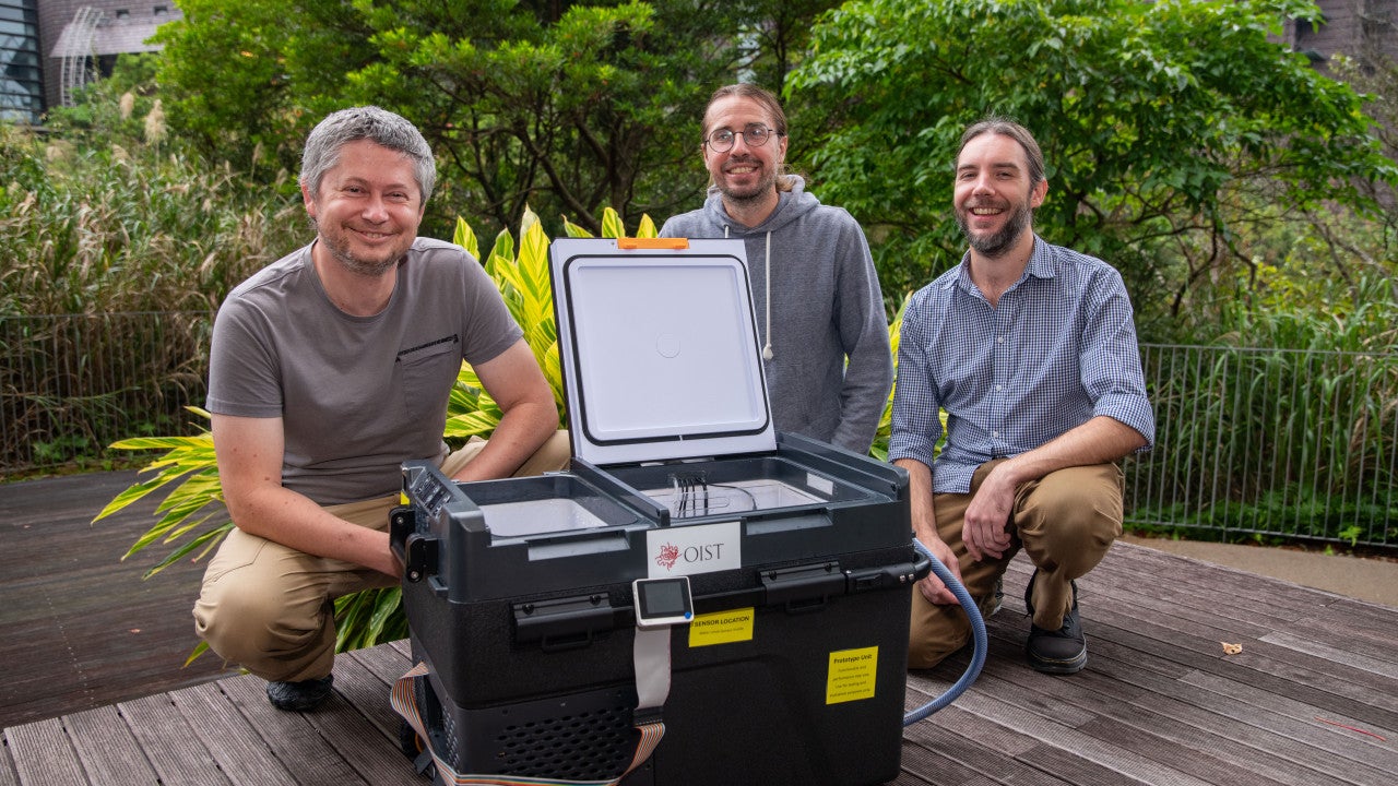 A photo of Peter Babiak, John Parker, and Zdenek Lajbner behind the newly developed cephalopod egg incubator, a large black box with wheels. 