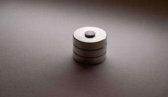 A photograph of a black graphite disk floating above a stack of three, round magnets.