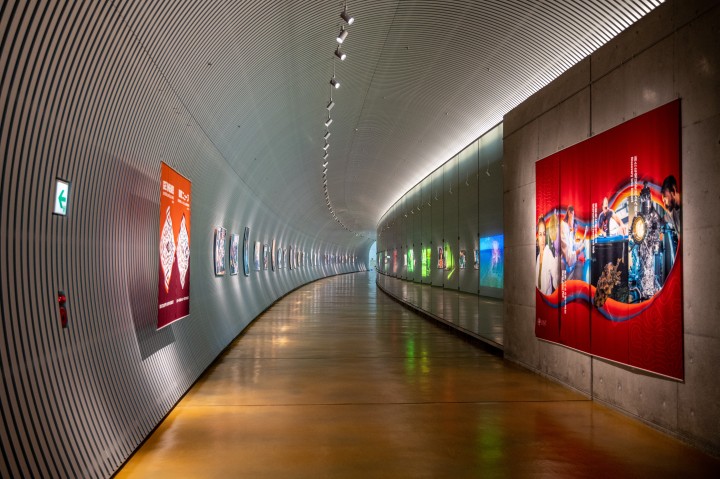 Picture of the Tunnel Gallery, the long cylindrical entrance to OIST where numerous pictures/videos are displayed on the walls.