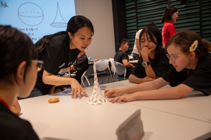 Girls and a lady gathering around a table looking at a tall white object