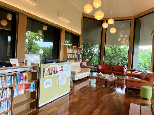 Large room with books, sofas, and big windows that show vegetation