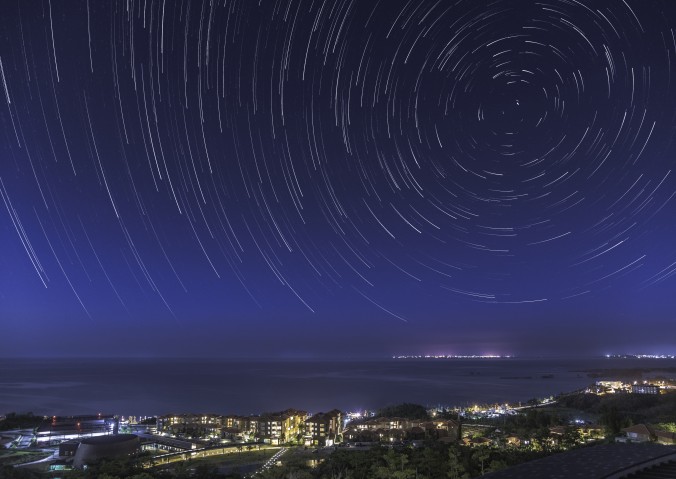 Time-lapse night photo of stars moving over Tancha Bay and OIST campus