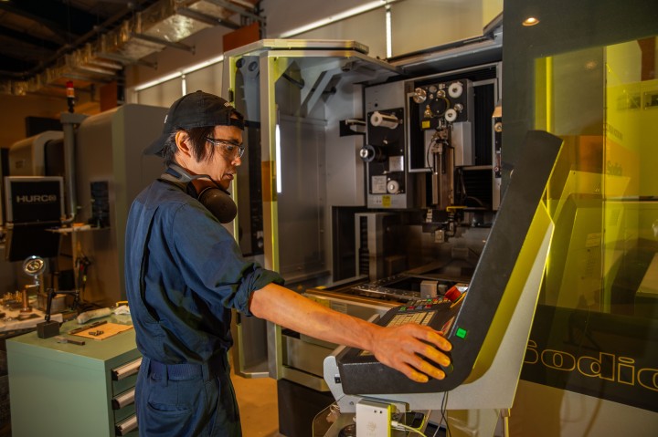 staff operating a Hurco wire cutter in working clothes. The machine is open and user is operating the control panel.