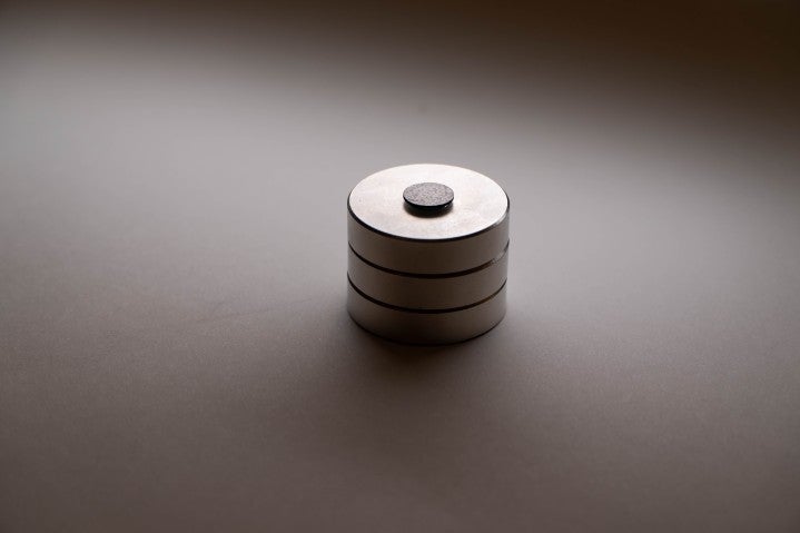 A photograph of a black graphite disk floating above a stack of three, round magnets.