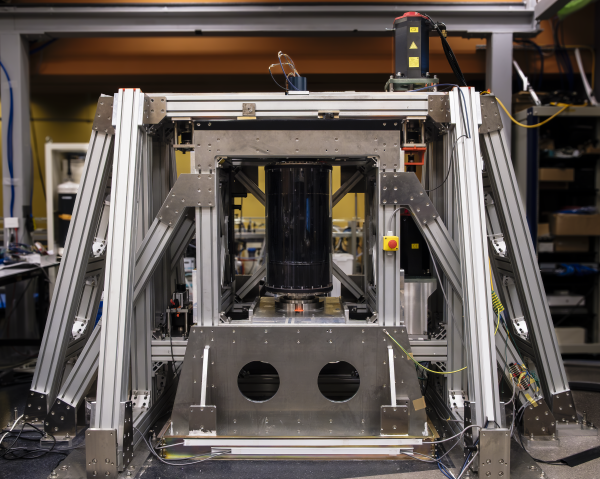 Photo of complicated, scientific instrumentation: a square frame surrounding another square frame, within which stands a black cylinder.