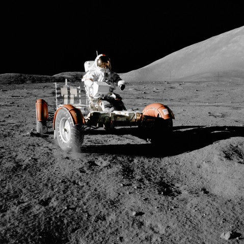 Color photograph of an astronaut driving a lunar rover on the Moon’s surface. 