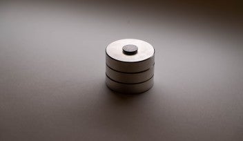 A photograph of a black graphite disk floating above a stack of three, round magnets.