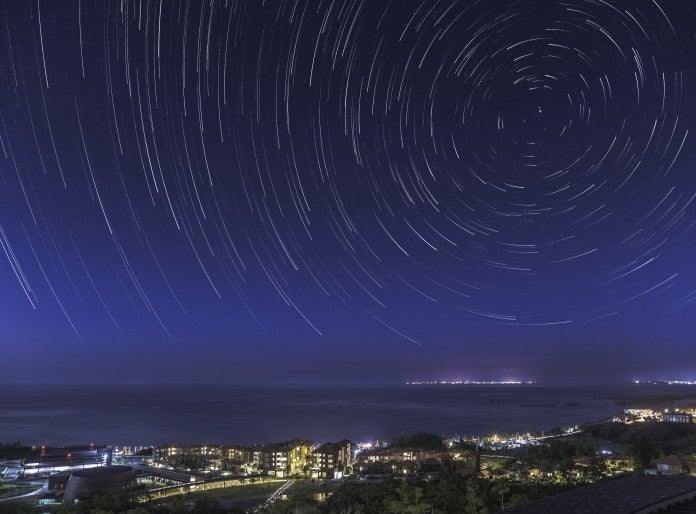 Time-lapse night photo of stars moving over Tancha Bay and OIST campus