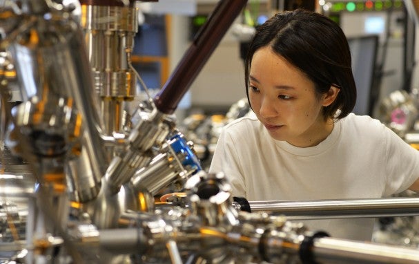 Woman on the right looks down and to the left at a large machine with plenty of pipes
