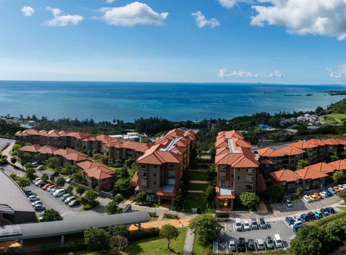 Aerial (drone) view of OIST's Village Center and entrance to the Tunnel Gallery, overlooking the ocean and a sunny sky with few clouds